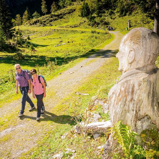 Wanderer vor einer Holzskulptur auf dem Schnitzlerweg auf der Axalp im Sommer