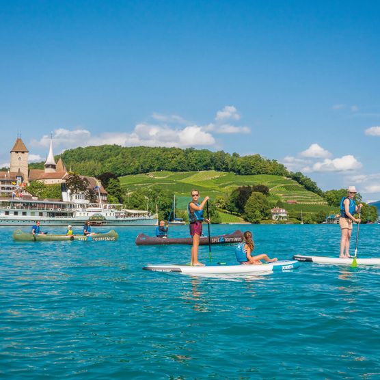 Freunde gleiten über das tiefblaue Wasser und geniessen die umliegende grüne Naturlandschaft und den Ausblick auf das Schloss Spiez