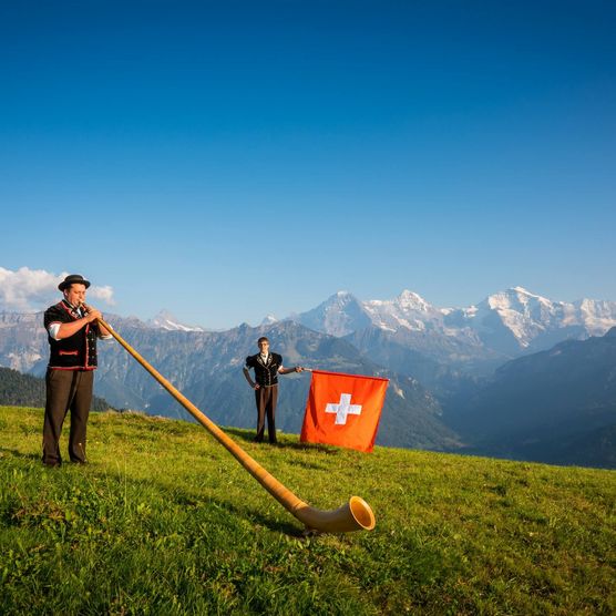 Ein Fahnenschwinger und ein Alphornbläser posieren auf Amisbühl bei Beatenberg vor Eiger, Mönch und Jungfrau