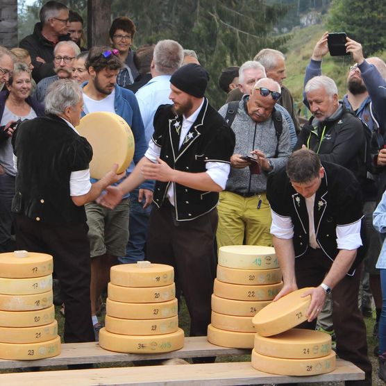 Käse wird von Älplern auf Holzbrettern aufgetürmt umgeben von Zuschauern