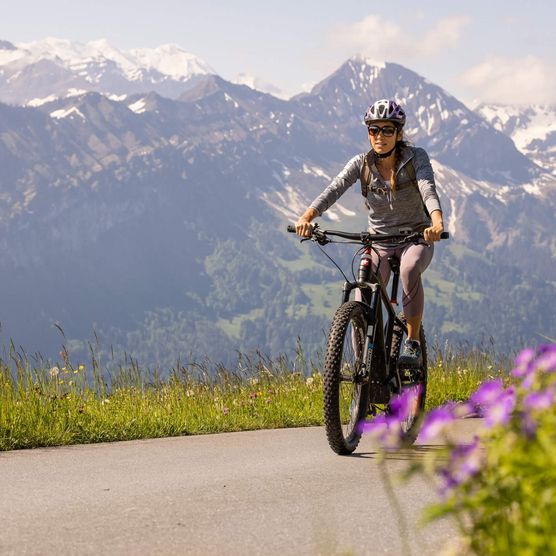 Frau fährt mit Bergkette im Hintergrund mit dem E-Bike auf das Niederhorn