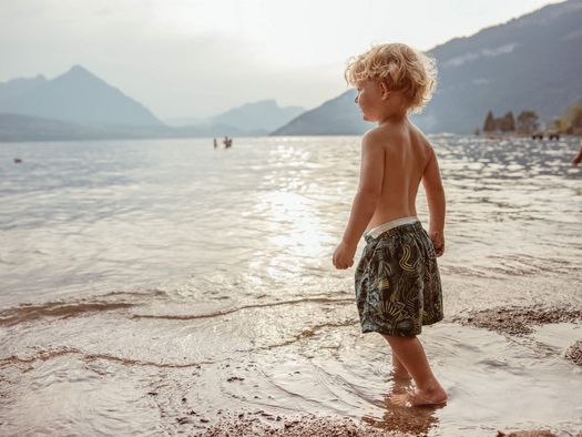 Kleiner Junge steht am Ufer des Thunersees beim Schülerbad Neuhaus und schaut Richtung Berge