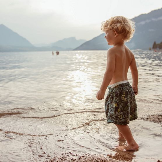 Kleiner Junge steht am Ufer des Thunersees beim Schülerbad Neuhaus und schaut Richtung Berge