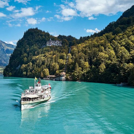 Schiff auf dem türkisfarbenen Brienzersee im Sommer mit dem Grandhotel Giessbach im Hintergrund