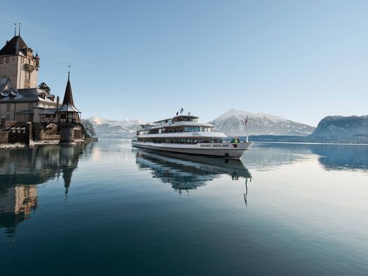 Schiff fährt im Winter neben dem Schloss Oberhofen über den spiegelglatten Thunersee