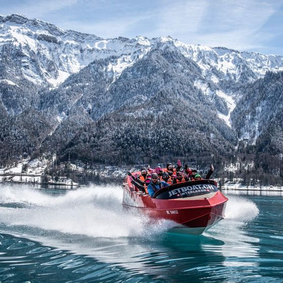 Jetboat unterwegs auf dem spiegelglatten Brienzersee im Winter mit verschneiten Wälder und Bergen