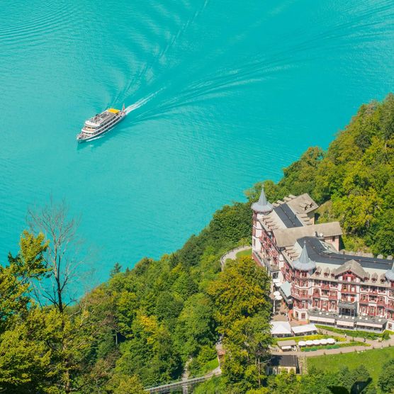 Ein Schiff auf dem türkisen Brienzersee und im grünen Wald das Grandhotel Giessbach