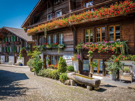 Ein mit Blumen geschmücktes Chalet und davor ein handgeschnitzer Brunnen