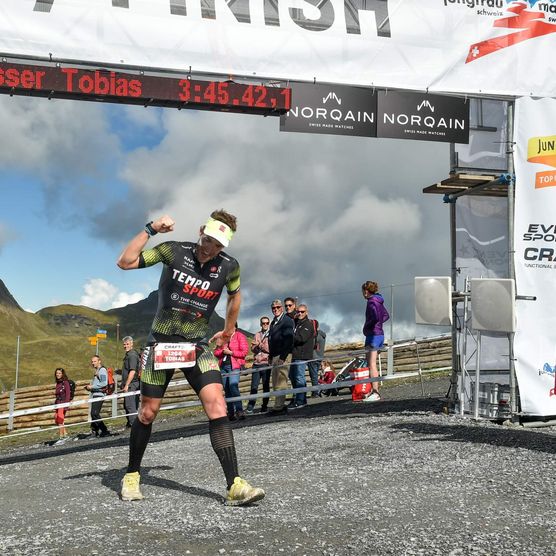 Der Läufer Tobias Giesser jubelt über seinen Einlauf im Ziel des Jungfrau-Marathons und seinen 26. Rang vor zwei Zieldamen in einer traditionellen Tracht