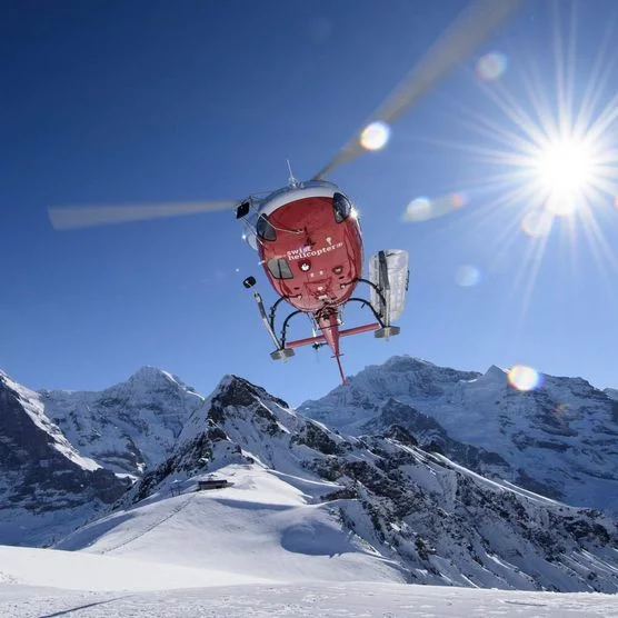 Ein Helikopter hebt ab umgeben von verschneiter Winterlandschaft mit Eiger, Mönch und Jungfrau im Hintergrund