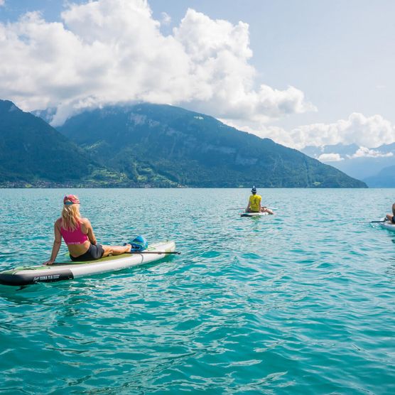 Drei Freunde relaxen auf dem Thunersee auf Stand Up Paddle Boards und geniessen den Blick auf die Bergwelt